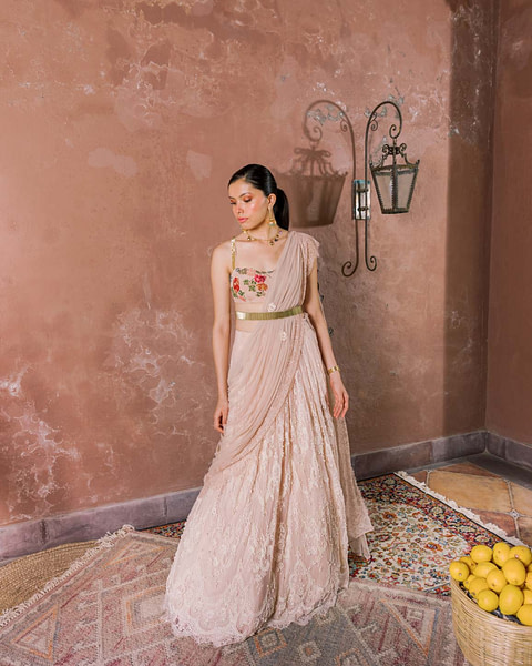 Gracefully clad in a lace-embellished saree with a floral blouse, a woman stands contemplatively beside a basket of lemons and an antique rug.