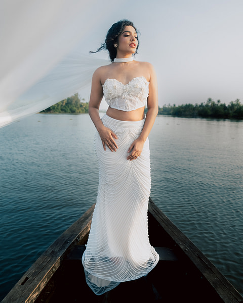 A bride in a strapless corset bridal gown with floral appliqués standing on a boat with a flowing veil and a serene lake in the background