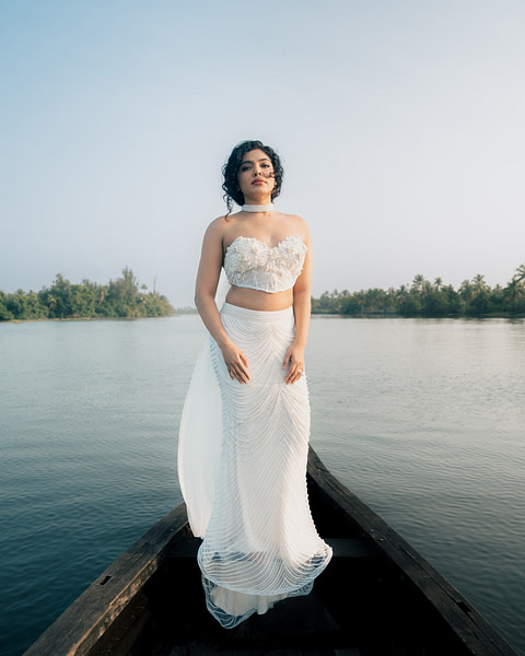 Frontal view of a bride on a boat wearing a strapless corset bridal gown with detailed beading, against a backdrop of calm waters and clear skies.