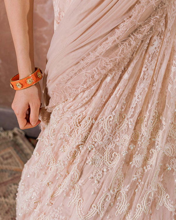 Close-up on the intricate detailing of a rose lace and pearl-embellished saree, paired with an orange floral belt, expressing delicate femininity.
