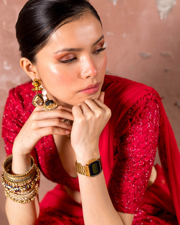 A contemplative woman in a detailed red ensemble gazes downward, her jewelry reflecting a rich cultural heritage.