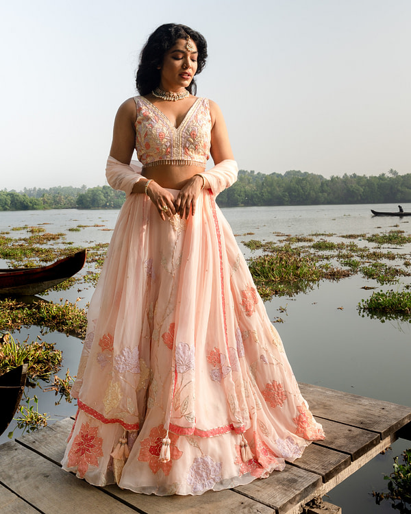Bride in a detailed Petal Blush Lehenga looking downwards, with delicate embroidery, on a tranquil lakeside setting.
